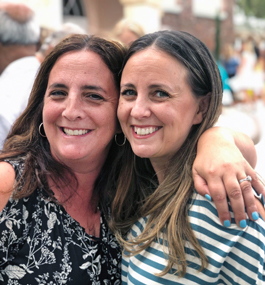 A close-up of two smiling women with the arms around each other's shoulders